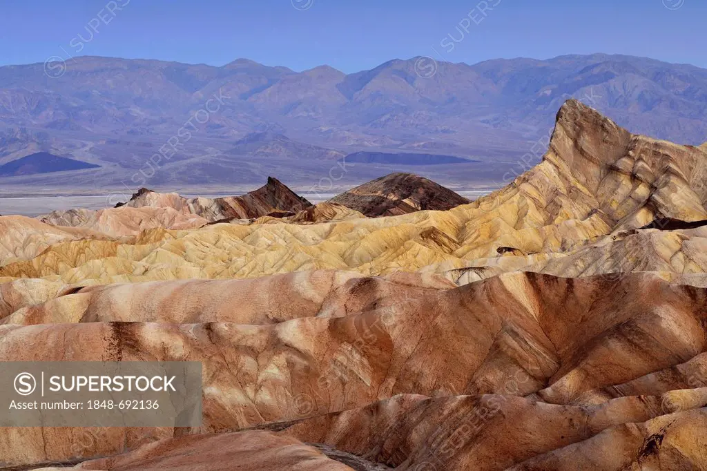 View from Zabriskie Point towards Manly Beacon with eroded rocks discoloured by minerals, with Panamint Range in the distance, dawn, Death Valley Nati...