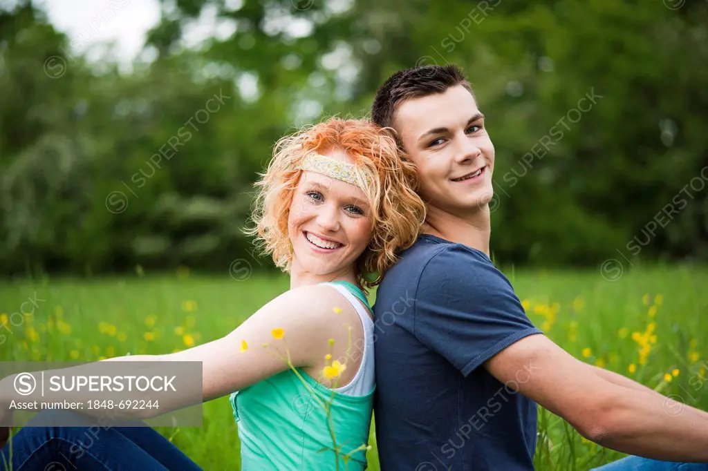 Smiling young couple sitting back to back on a meadow