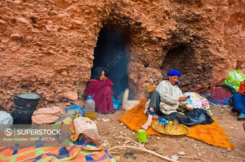 Cave dwelling nomads in front of their cave dwelling, a man is crushing sugar for their tea, High Atlas Mountains, Morocco, Africa