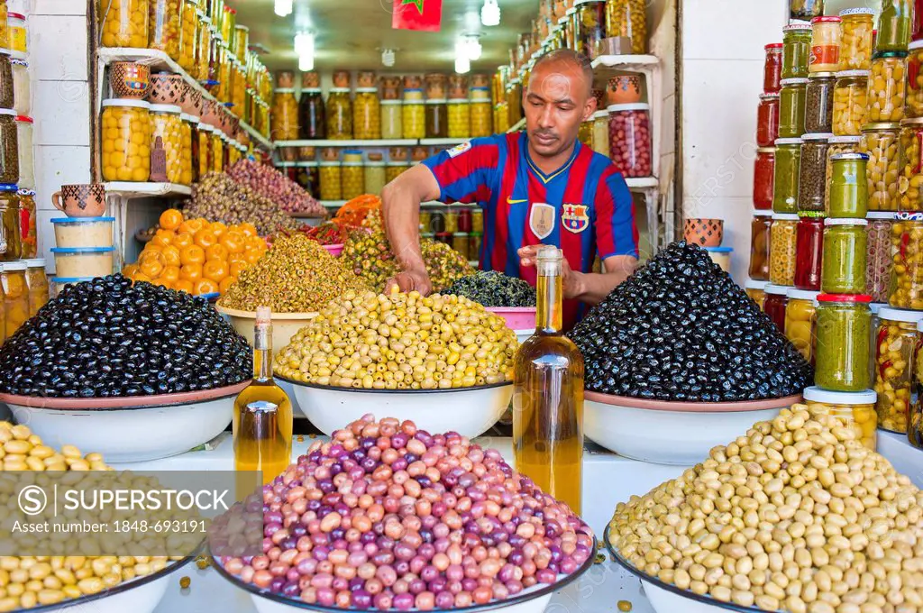 Merchant offering different olives, olive oil in dishes and glasses for sale at his stand, souk, bazaar, Marrakesh, Morocco, Africa