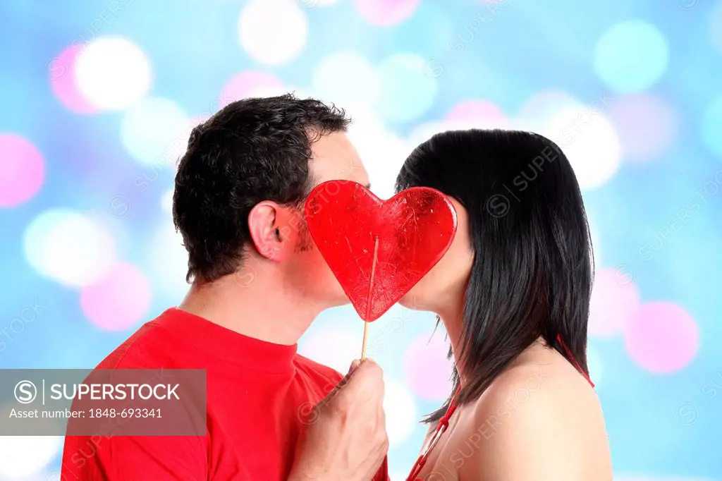 Young couple kissing behind a heart-shaped lollipop