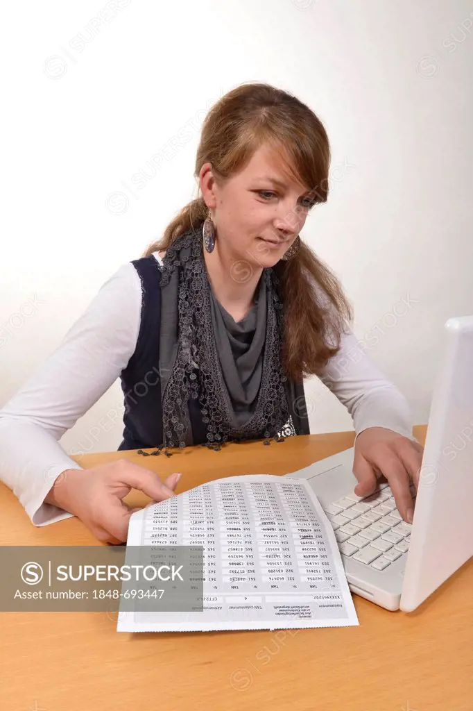 Woman working on a laptop computer with a TAN-list for online banking