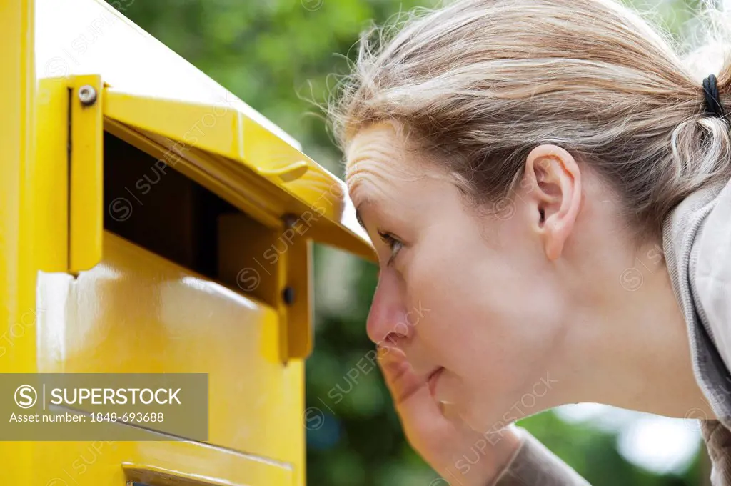 Young woman looking curiously into a postbox