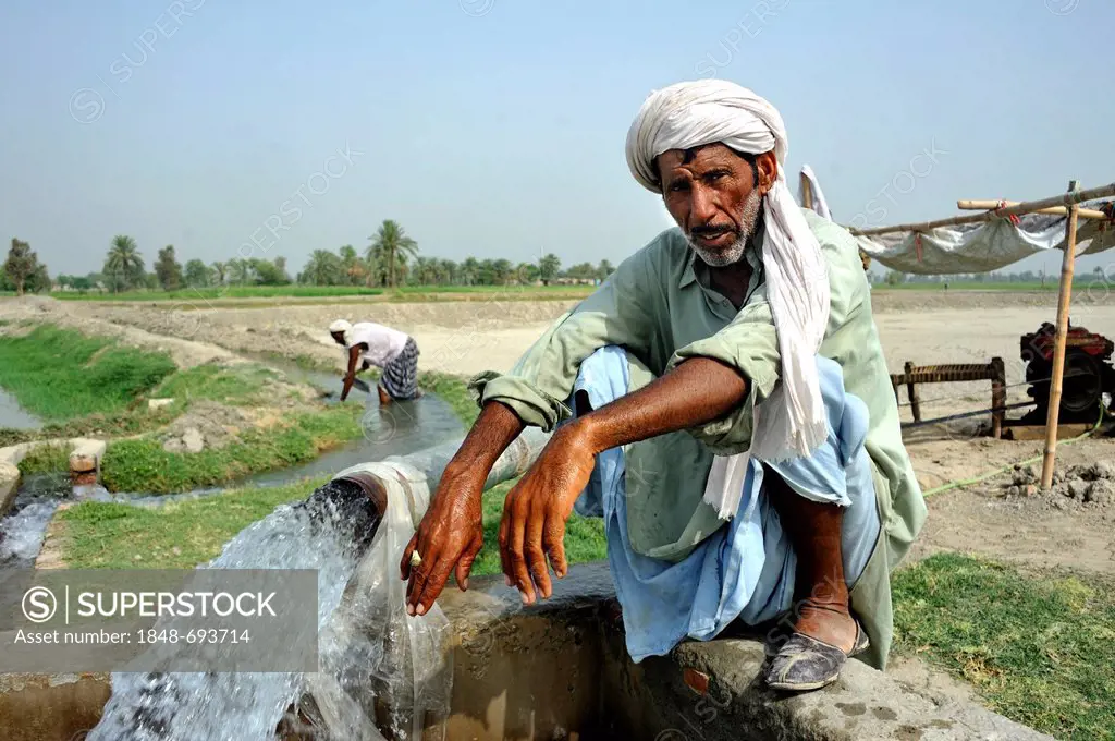 Farmer squatting on the catchment of a spring that is feeding an agricultural irrigation canal, Basti Lehar Walla village, Punjab, Pakistan, Asia