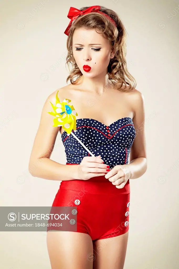 Young woman wearing hot pants with a red bow in her hair blowing against yellow pinwheel, pin-up