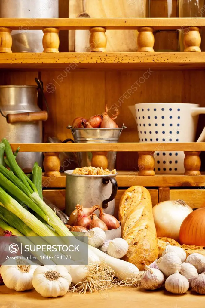 Different types of onions and garlic, and onion bread lying on a table, a shelf with spices at the back