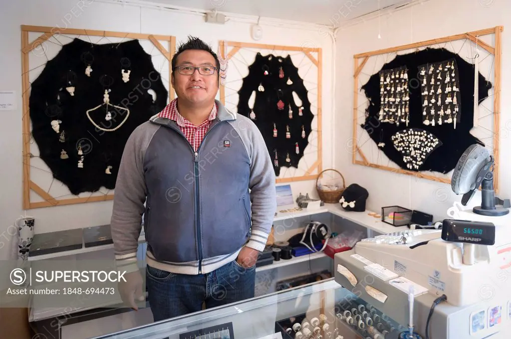 Inuit man standing in front of a jewellery display in the souvenir shop of the tourist office, Tasiilaq or Ammassalik, East Greenland, Greenland