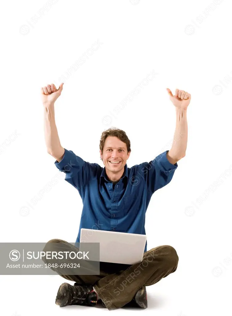 Man sitting cross-legged on floor with a laptop, cheering