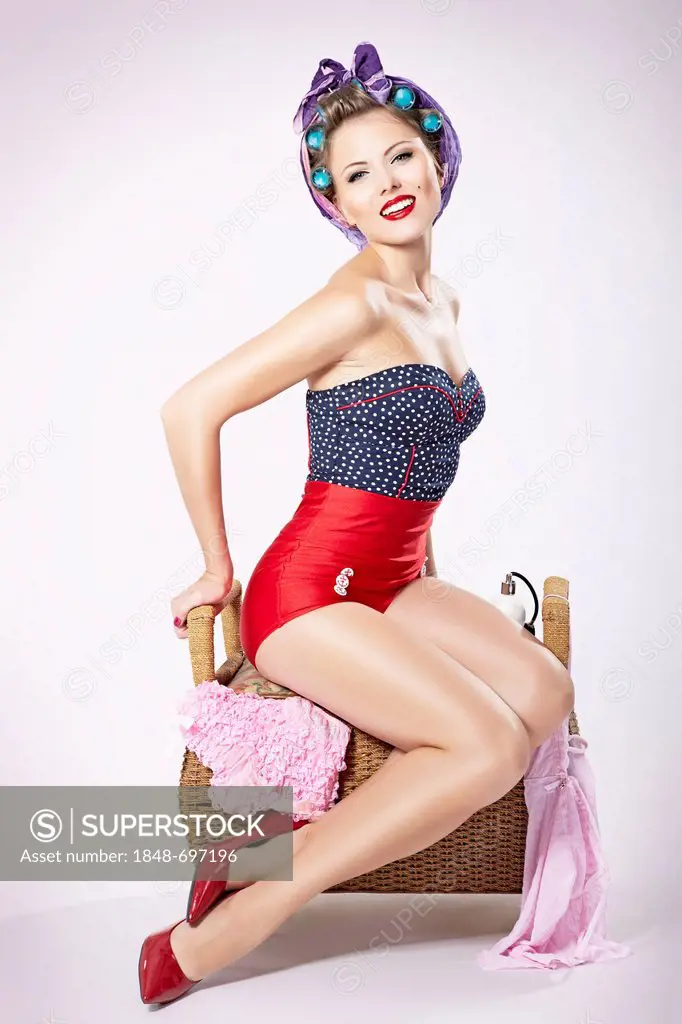 Young woman wearing hair curlers and hot pants sitting on a laundry basket, pin-up