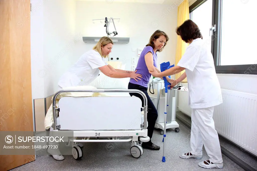 Nurses assisting a patient trying to walk with walking aids, mobilisation after an operation in a hospital