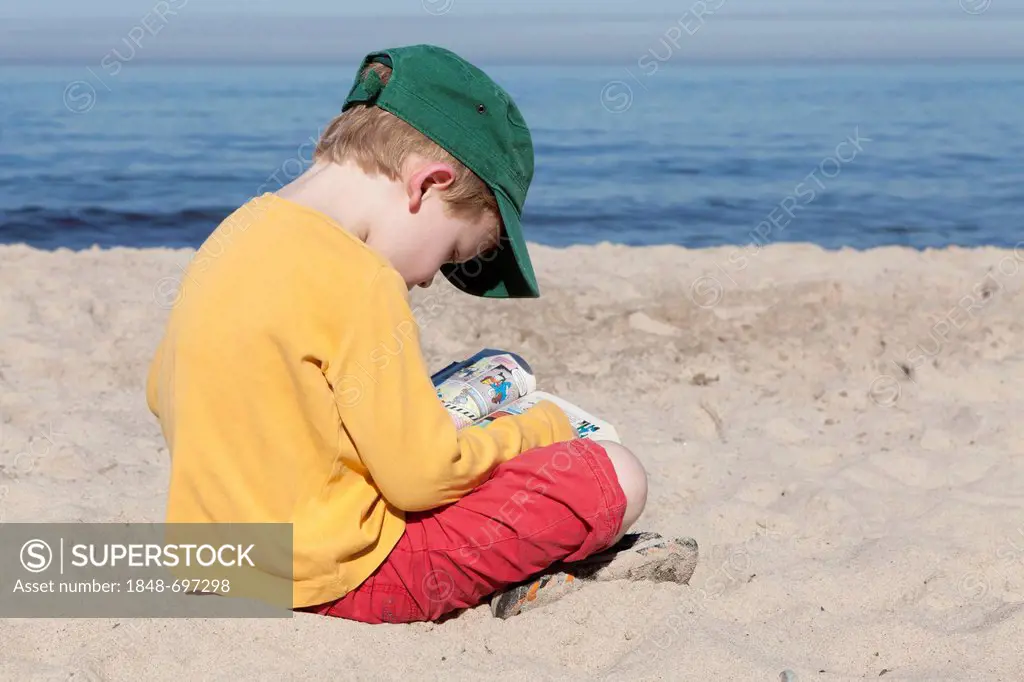 Young boy reading on a beach, Kuehlungsborn-West, Mecklenburg-Western Pomerania, Germany, Europe