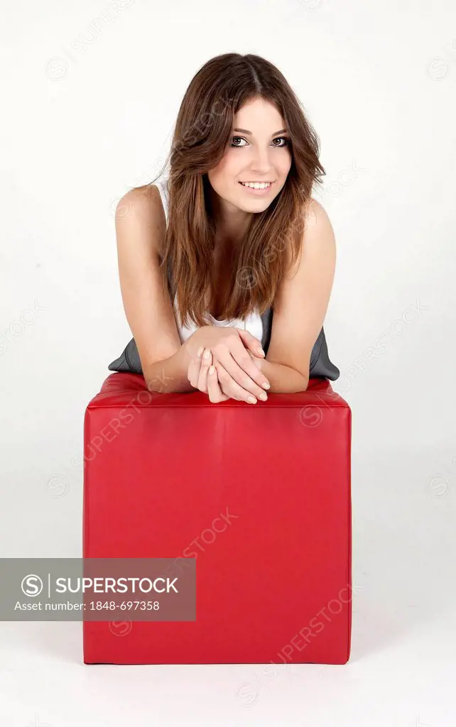 Smiling young woman leaning on a red cube