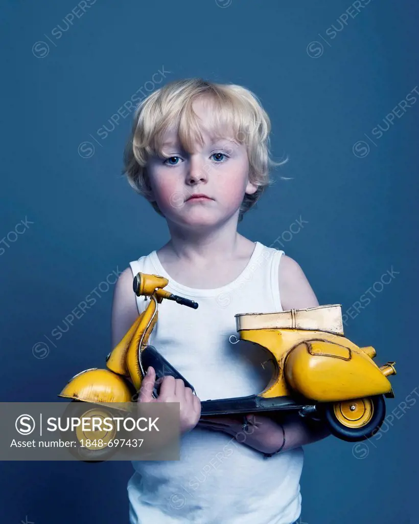 Five-year-old boy holding a toy Vespa scooter, gift, sad face
