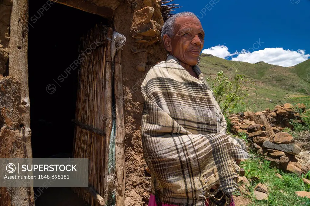 Old Basotho woman wearing a traditional dress standing in front of a hut, Drakensberg, Kingdom of Lesotho, southern Africa