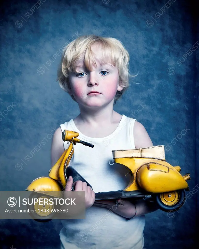 Five-year-old boy holding a toy Vespa scooter, gift, sad face