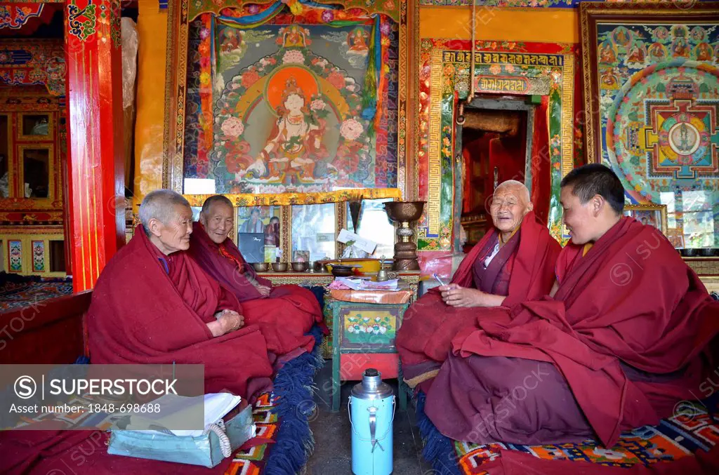 Four Tibetan nuns in red robes sitting in the assembly hall of the nunnery in the mountains of Reting Monastery, Mount Gangi Rarwa, Himalayas, Lhundru...