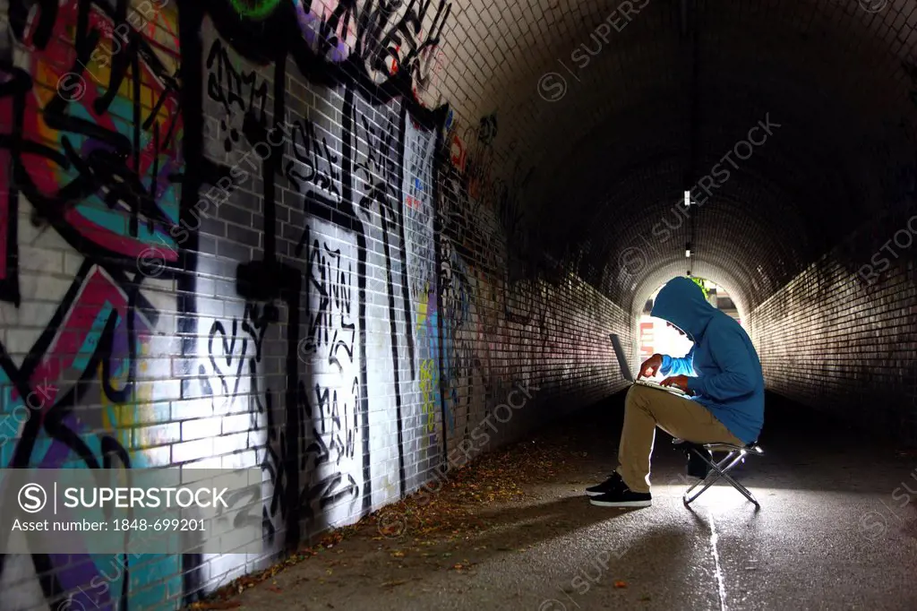 Man surfing on a laptop computer in a pedestrian tunnel, symbolic image for computer hacking, computer crime, cybercrime, data theft