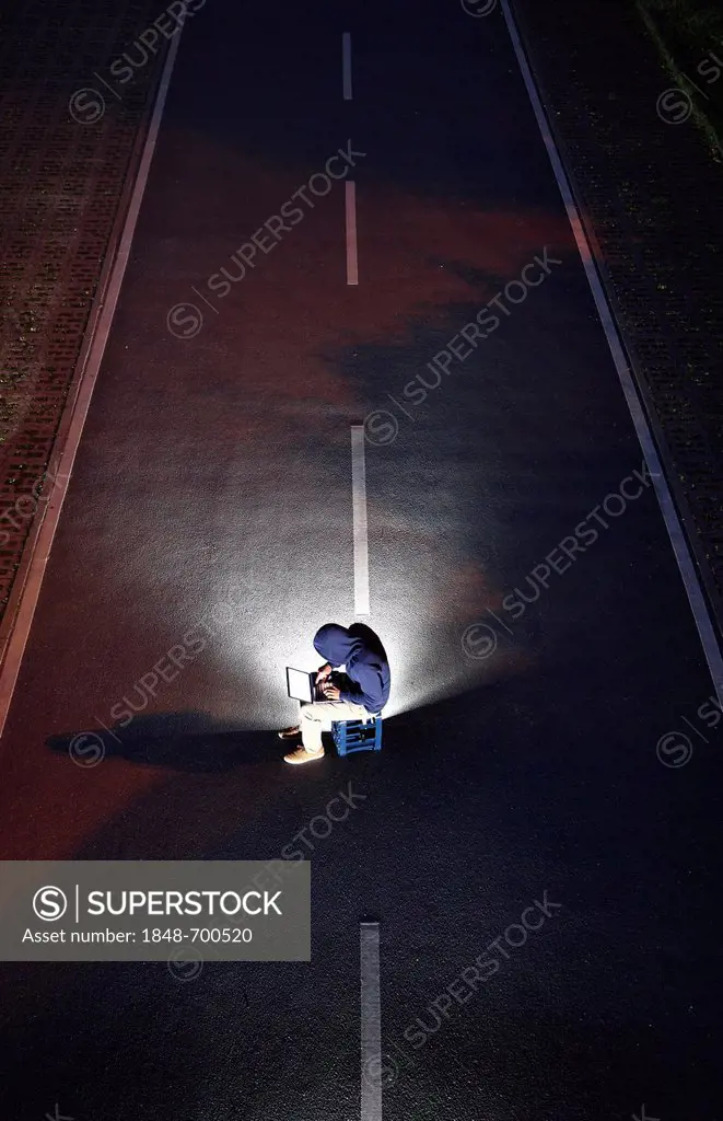 Man surfing on a laptop computer at night in the middle of the street, symbolic image for computer hacking, computer crime, cybercrime, data theft