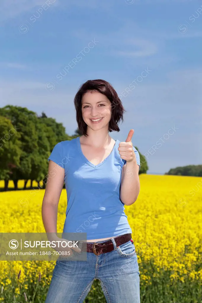Young woman standing in front of a field of rape, Swabian Alb, Baden-Wuerttemberg, Germany, Europe