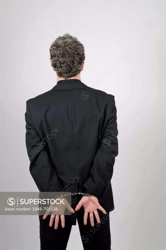 Businessman wearing a black suit, his hands handcuffed behind his back