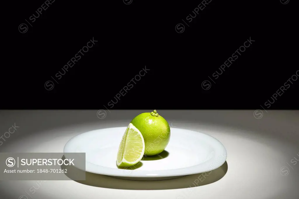 Limes (Citrus latifolia), whole and sliced, on a white plate
