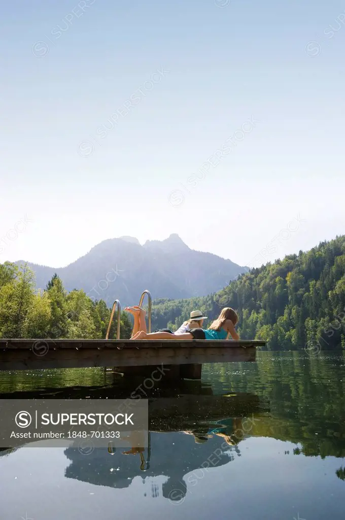 Young women lying on a landing stage on Lake Schwansee near Fuessen, Allgaeu region, Bavaria, Germany, Europe