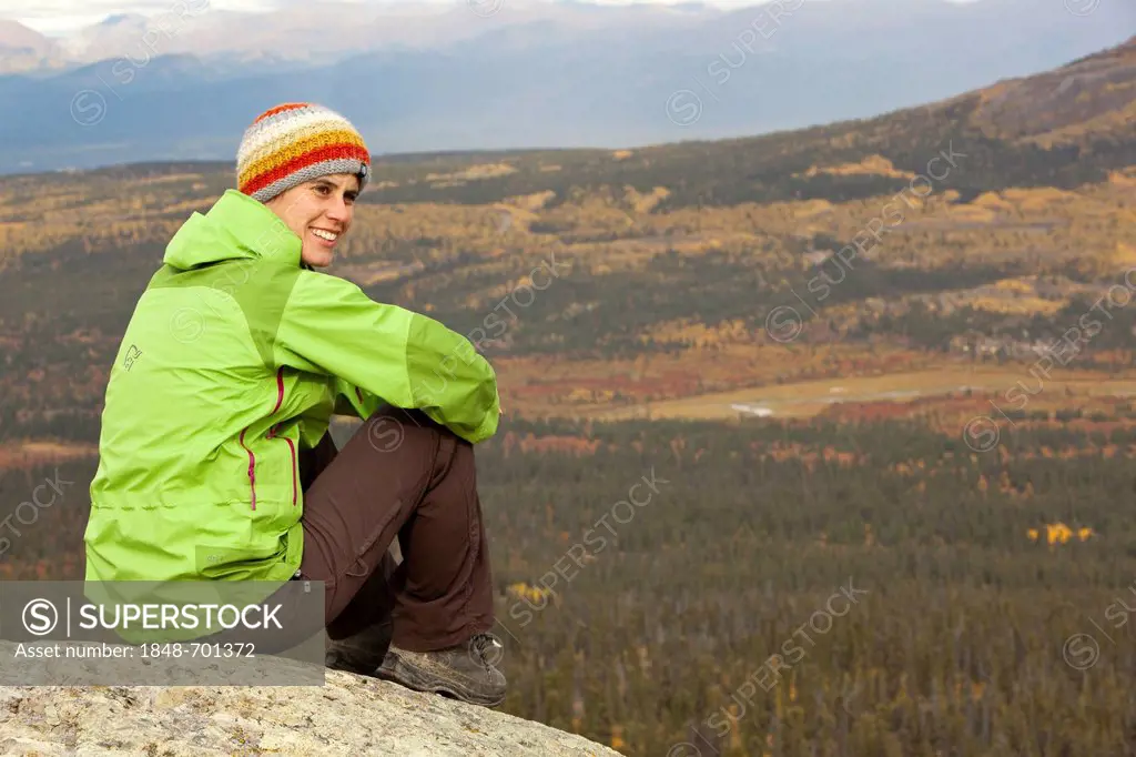 Young woman sitting on a rock on a mountain, resting, enjoying view, subalpine tundra, Indian summer, lautumn, near Fish Lake, Yukon Territory, Canada
