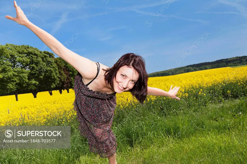 Woman standing with outstretched arms in front of a field of rape, Swabian Alb, Baden-Wuerttemberg, Germany, Europe