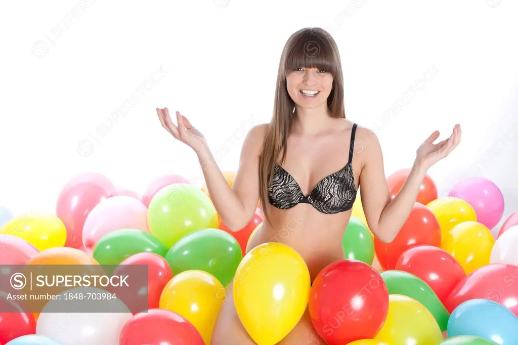 Young woman wearing lingerie sitting between colourful balloons and beaming with joy
