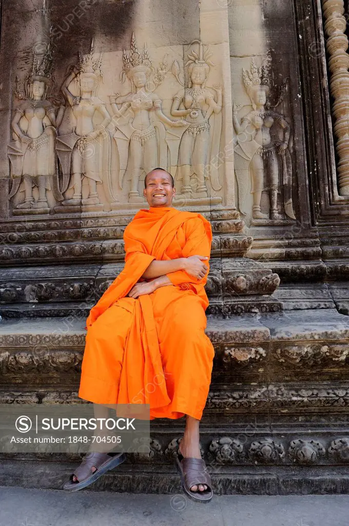 Buddhist monk in the centre of Angkor Wat sitting in front of a relief depicting Apsara from Hindu mythology, Cambodia, Southeast Asia, Asia