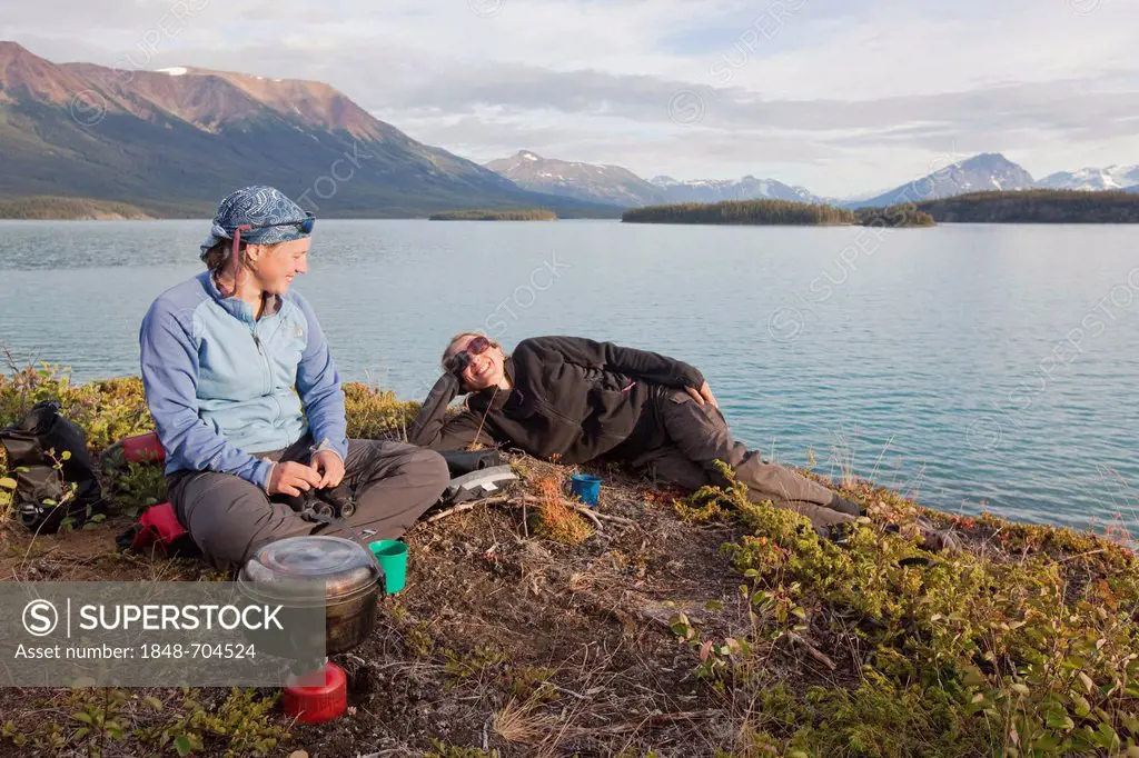 Two young women cooking on a camping stove, relaxing, Atlin Lake, British Columbia, Canada, America