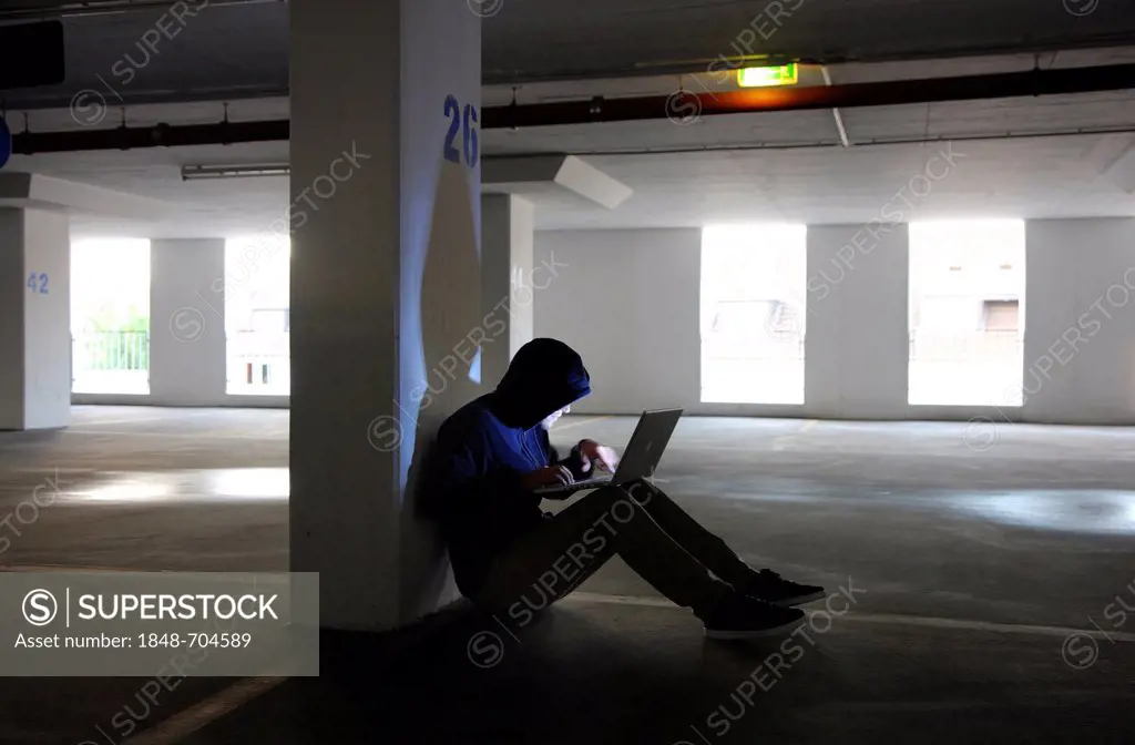 Man surfing on a laptop computer in an empty multi-storey car park, symbolic image for computer hacking, computer crime, cybercrime, data theft