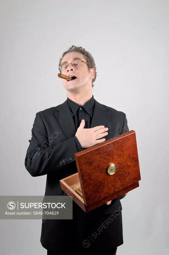 Businessman wearing a black suit with a cigar in his mouth holding a humidor, cigar box