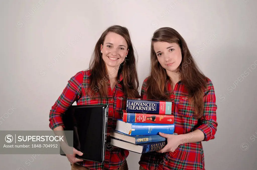Twin sisters, one holding a laptop, the other holding a stack of books