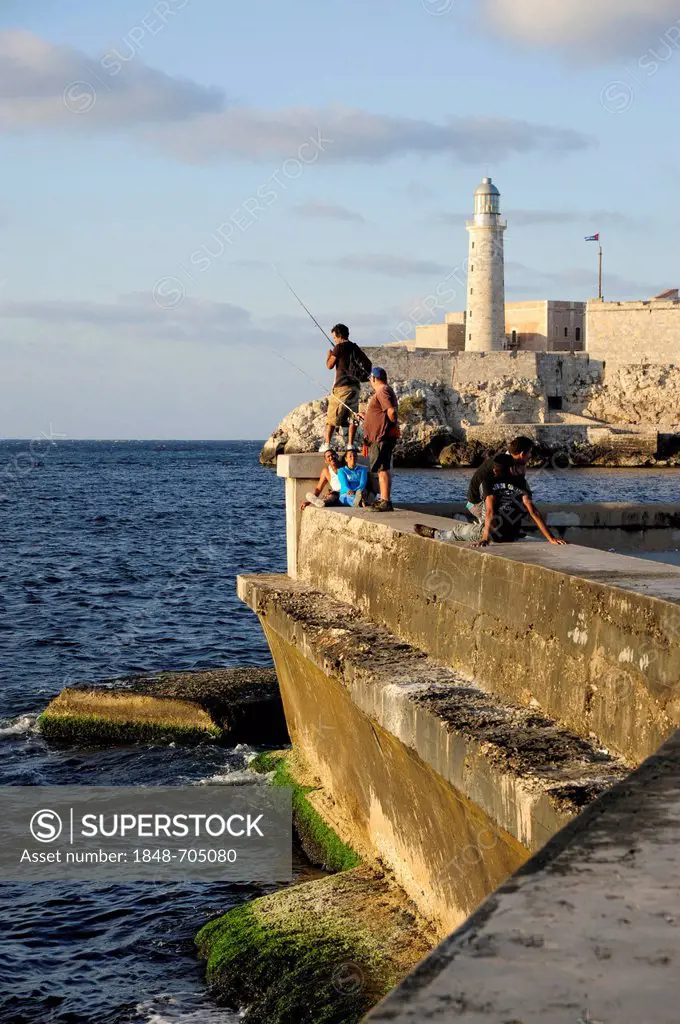 On the Malecon sea wall, Avenida de Antonio Maceo, a boulevard along the city centre of Havana, Centro Habana, with a lighthouse and a fort at the har...