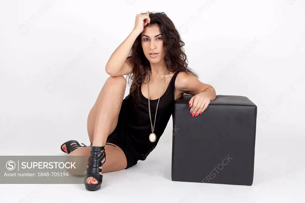 Young woman wearing a black top, hot pants and high heels posing with a black cube seat