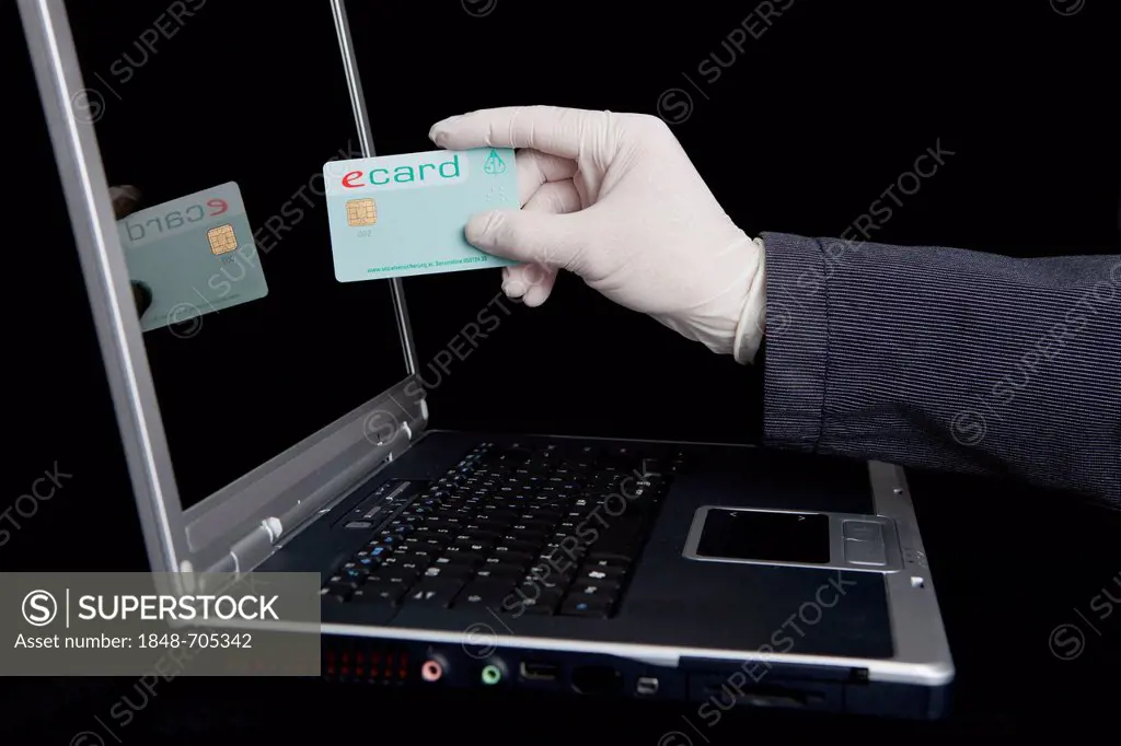 Hacker using a laptop, holding a health insurance card, symbolic image for welfare fraud