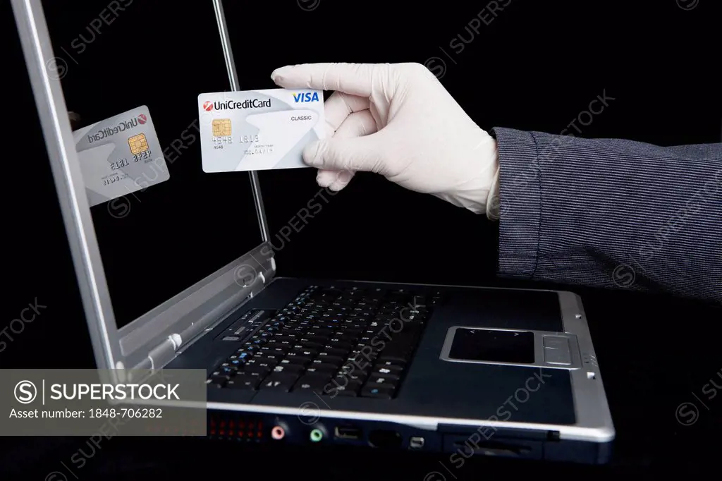 Hacker using a laptop, holding a Visa card and wearing latex gloves to leave no traces, symbolic image for Internet crime