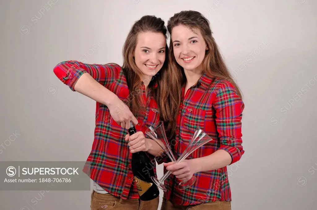 Twin sisters opening a bottle of sparkling wine