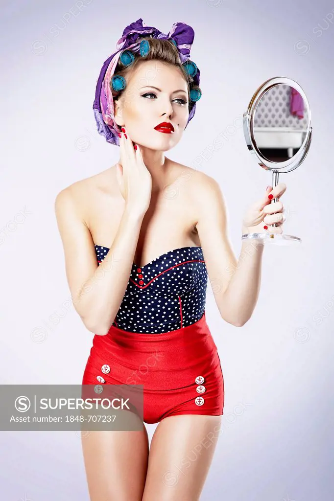 Young woman wearing hair curlers and hot pants looking in a hand mirror, pin-up