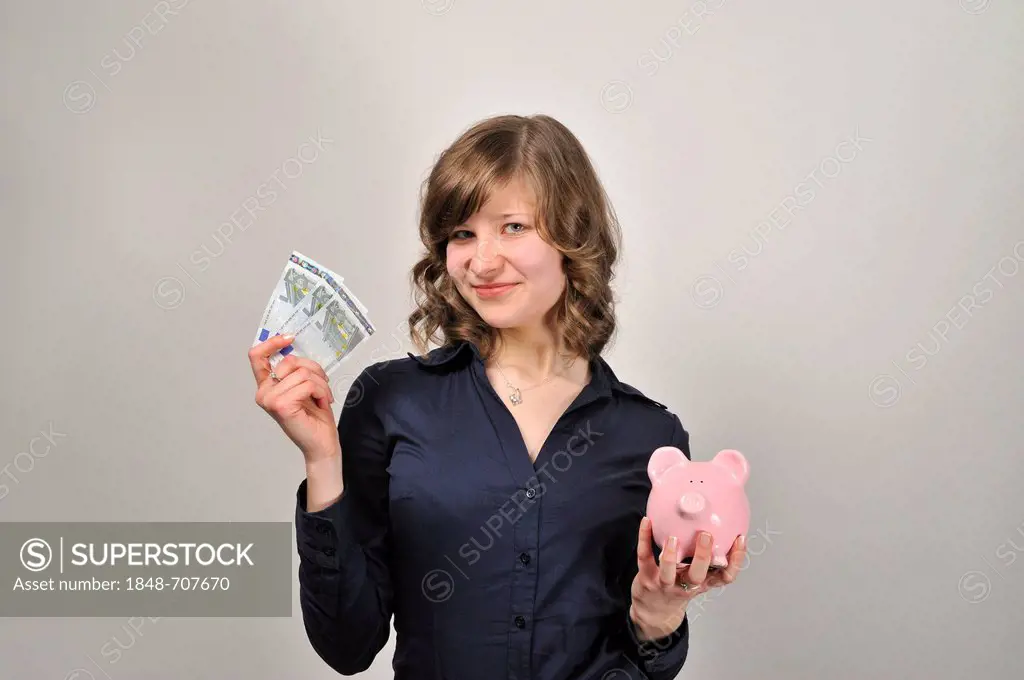 Young woman, 20, holding three 5 euro banknotes and a pink piggy bank