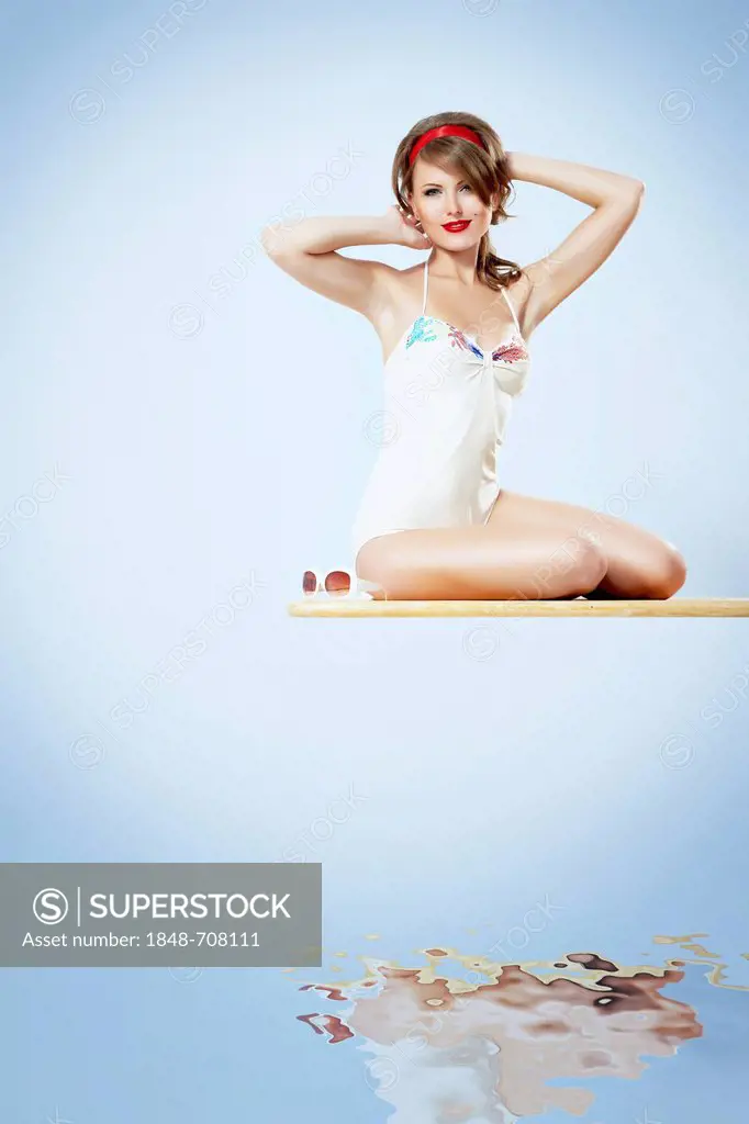 Young woman wearing a white bathing suit sitting on a diving board, pin-up