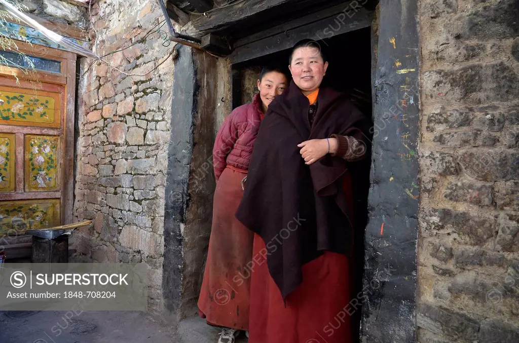 Two Tibetan nuns standing outside the monastery kitchen of the nunnery in the mountains of Reting Monastery, Mount Gangi Rarwa, Himalayas, Lhundrup Co...