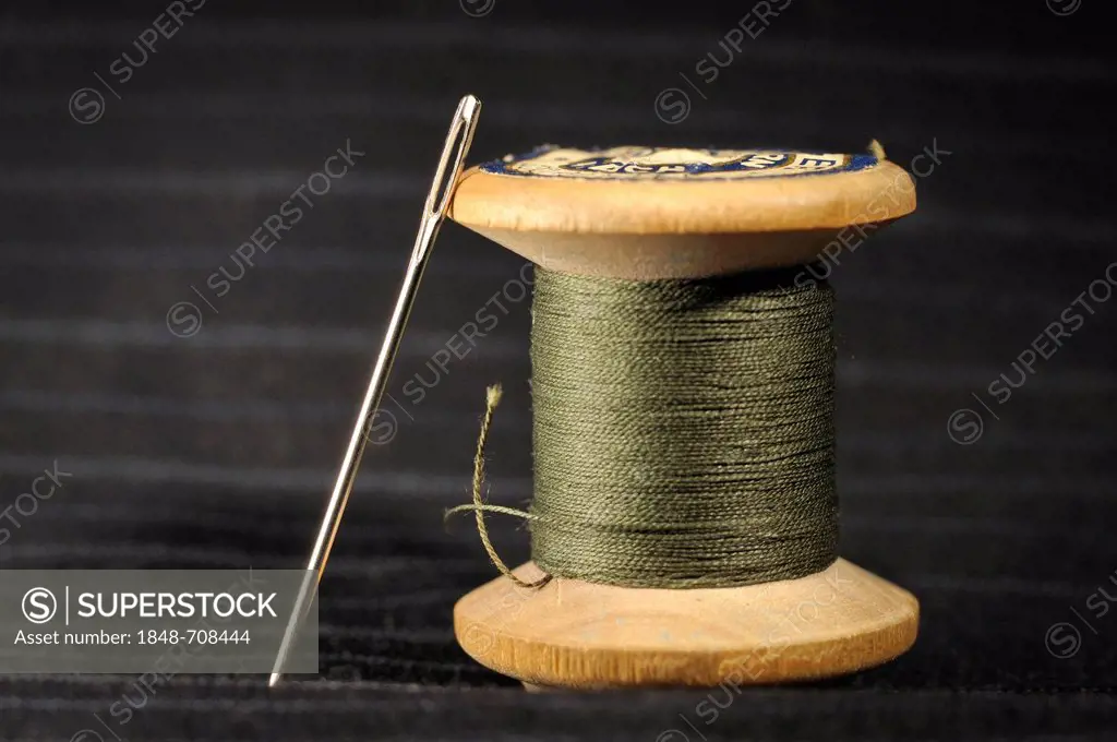 Wooden spool with green thread and darning needle, on black striped cotton