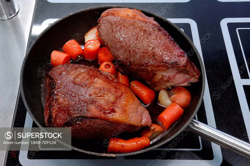 Roast beef with carrots being cooked in a pan on an induction cooker