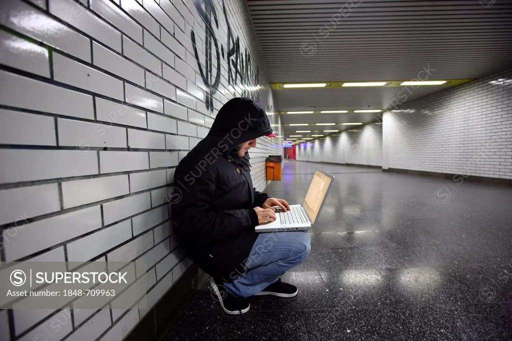 Hacker surfing on a laptop computer in a subway passage, symbolic image for computer hacking, computer crime, cybercrime, data theft