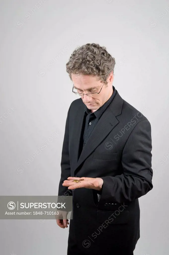 Businessman wearing a black suit gloomily looking at the few coins in his hand