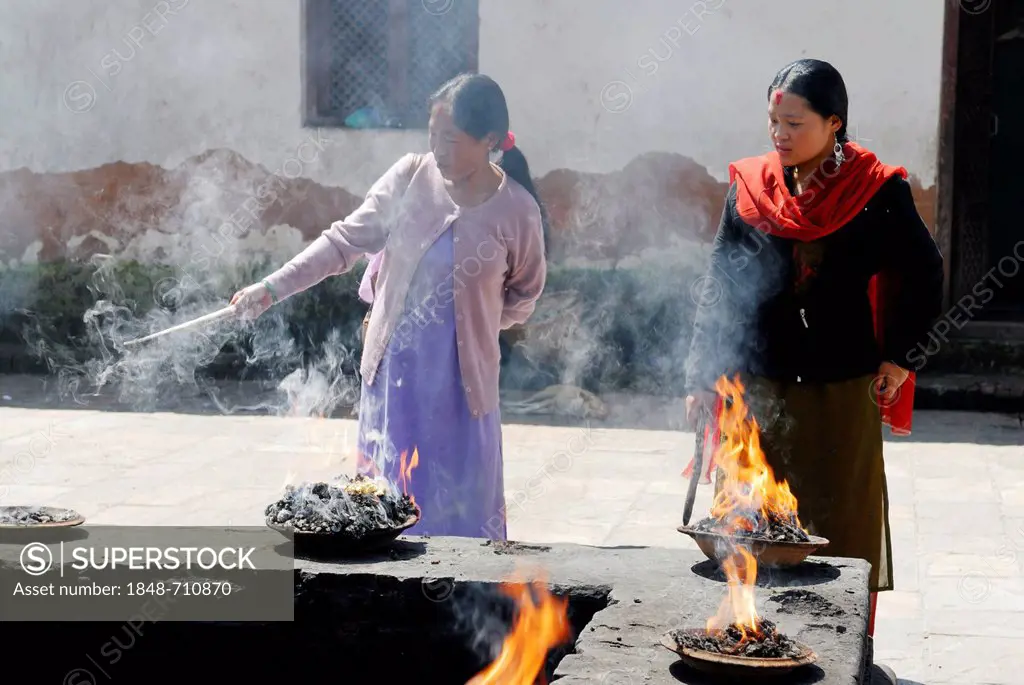 Female worshippers igniting fire in dishes, Pashupatinath, Kathmandu, Nepal, Asia