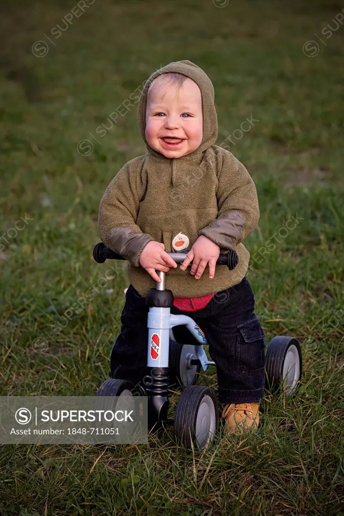 Young boy, 1, seated on a four-wheel Puky push bike, learning to walk, looking happy, Germany