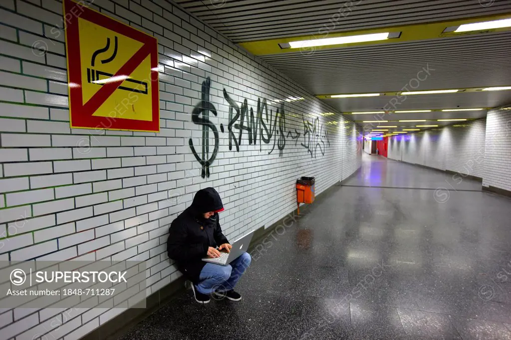 Hacker surfing on a laptop computer in a subway passage, symbolic image for computer hacking, computer crime, cybercrime, data theft